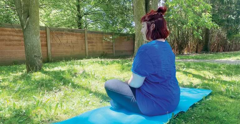 Young woman meditating on yoga mat outdoors.