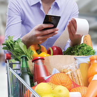 Someone holding a grocery bill, using a phone, in front of produce.