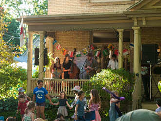 Photo of musicians playing on a porch with children dancing in the yard