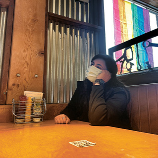 Photo of a woman sitting alone at a restaurant table wearing a mask
