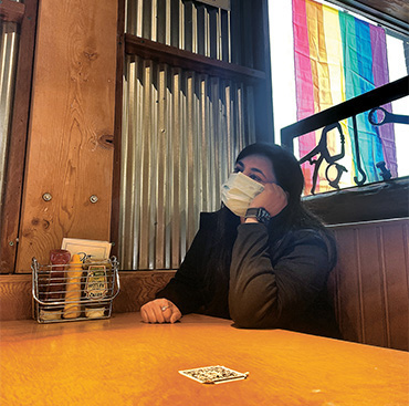 Photo of a woman sitting alone at a restaurant table wearing a mask