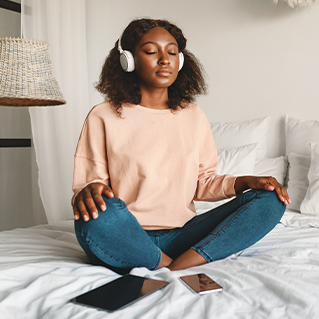 A stock image of a woman meditating while wearing headphones.